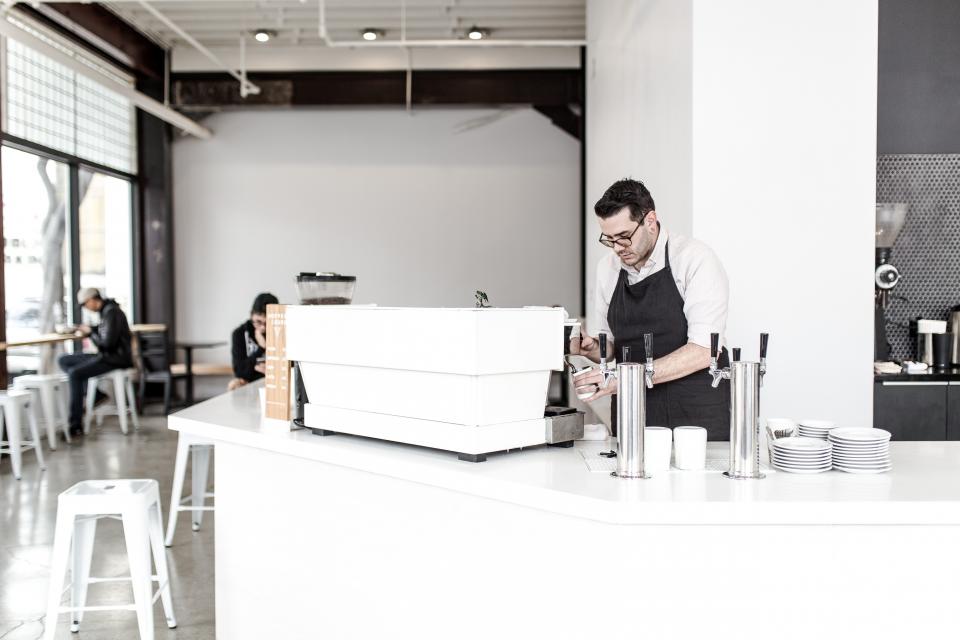 A barista working behind the counter of a bright, white cafe