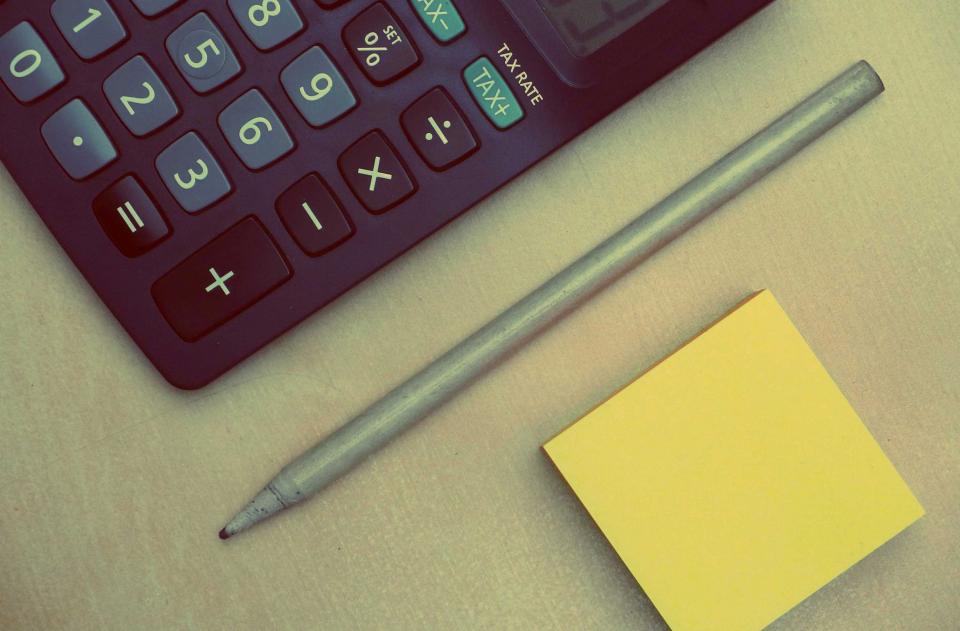 A calculator, a pencil and a yellow sticky note on a desk