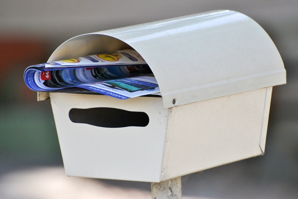 A white mailbox stuffed with advertising flyers