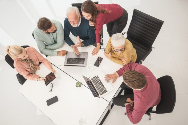 A group of colleagues working with laptops around a white table, seen from above