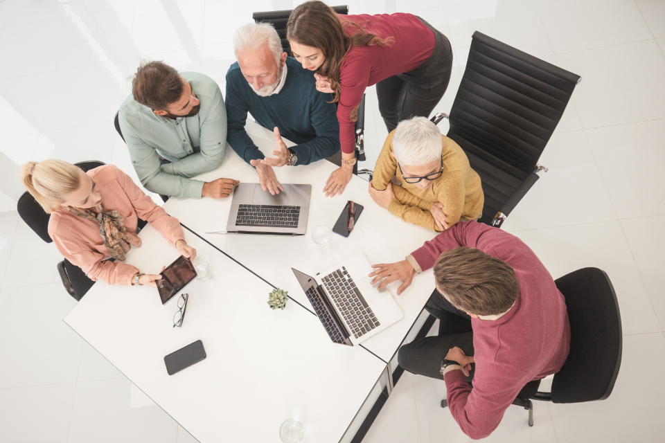 A group of colleagues working with laptops around a white table, seen from above