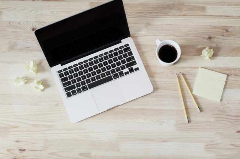 A laptop, a cup of coffee, pencils and sticky notes on a wooden desk