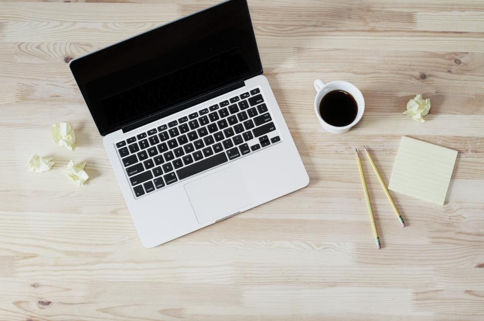 A laptop, a cup of coffee, pencils and sticky notes on a wooden desk